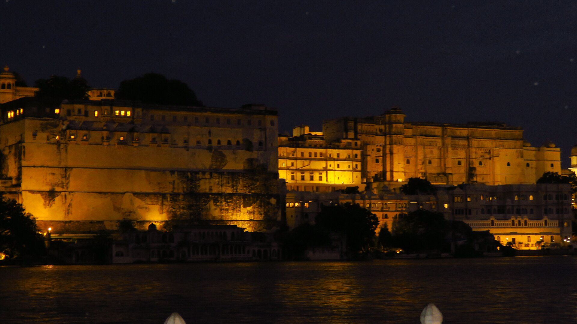 The City Palace of Udaipur floodlit gold above the dark water of Lake Pichola, its ranges and balconies picked out against a night sky