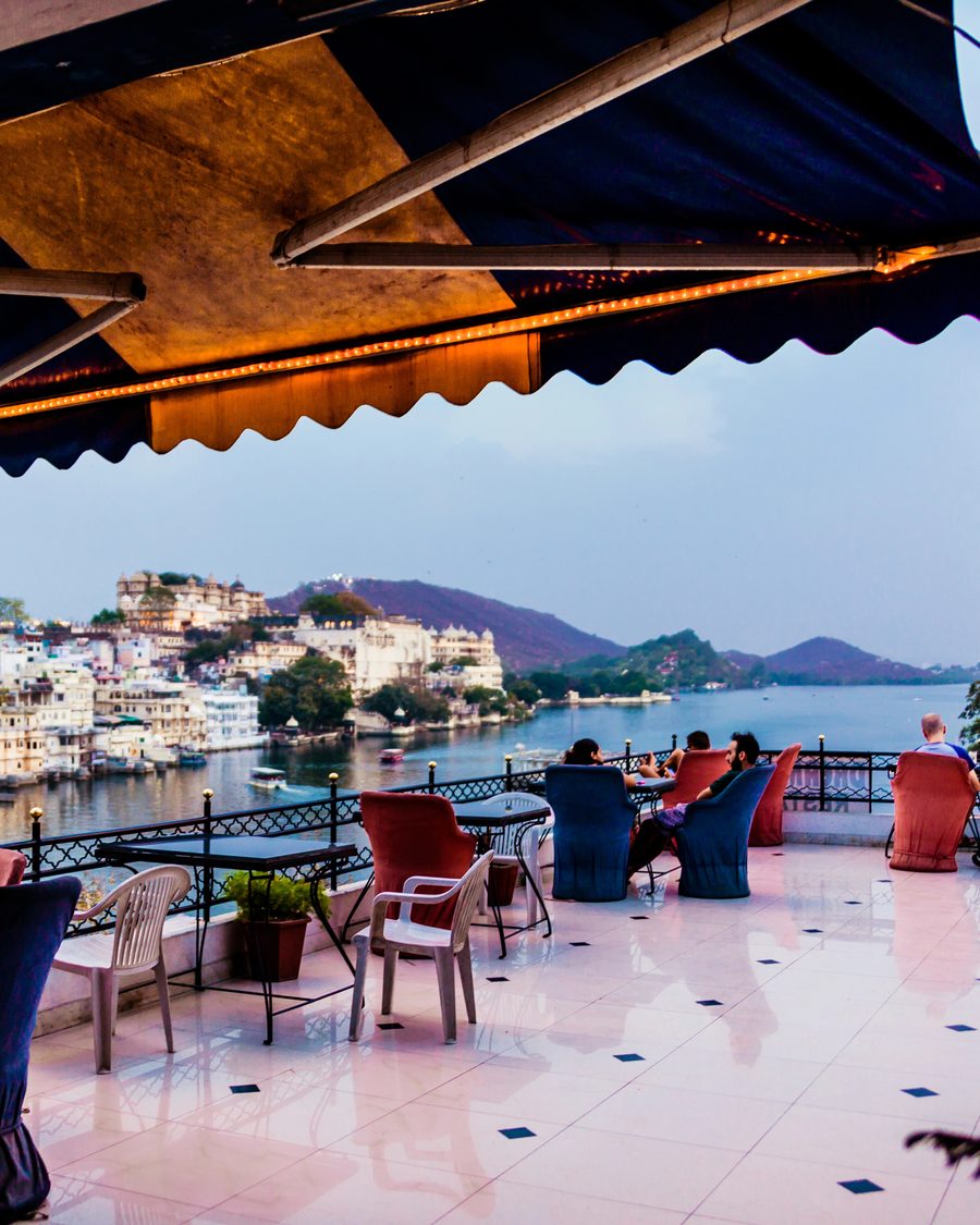 A lakeside rooftop terrace at dusk in Udaipur, chairs set out and lanterns lit above Lake Pichola